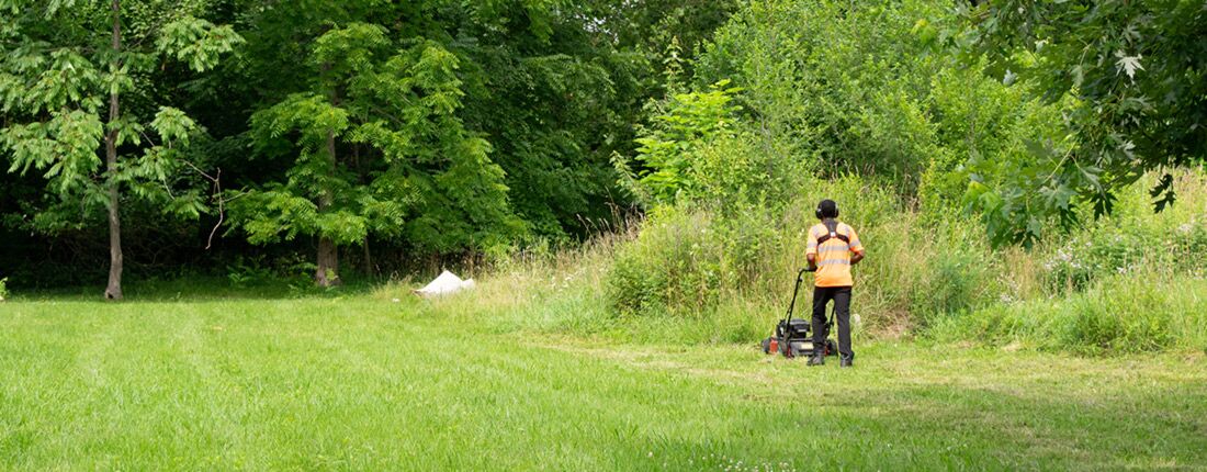 person-mowing-vacant-lot A person in a reflective orange vest mows a vacant lot.